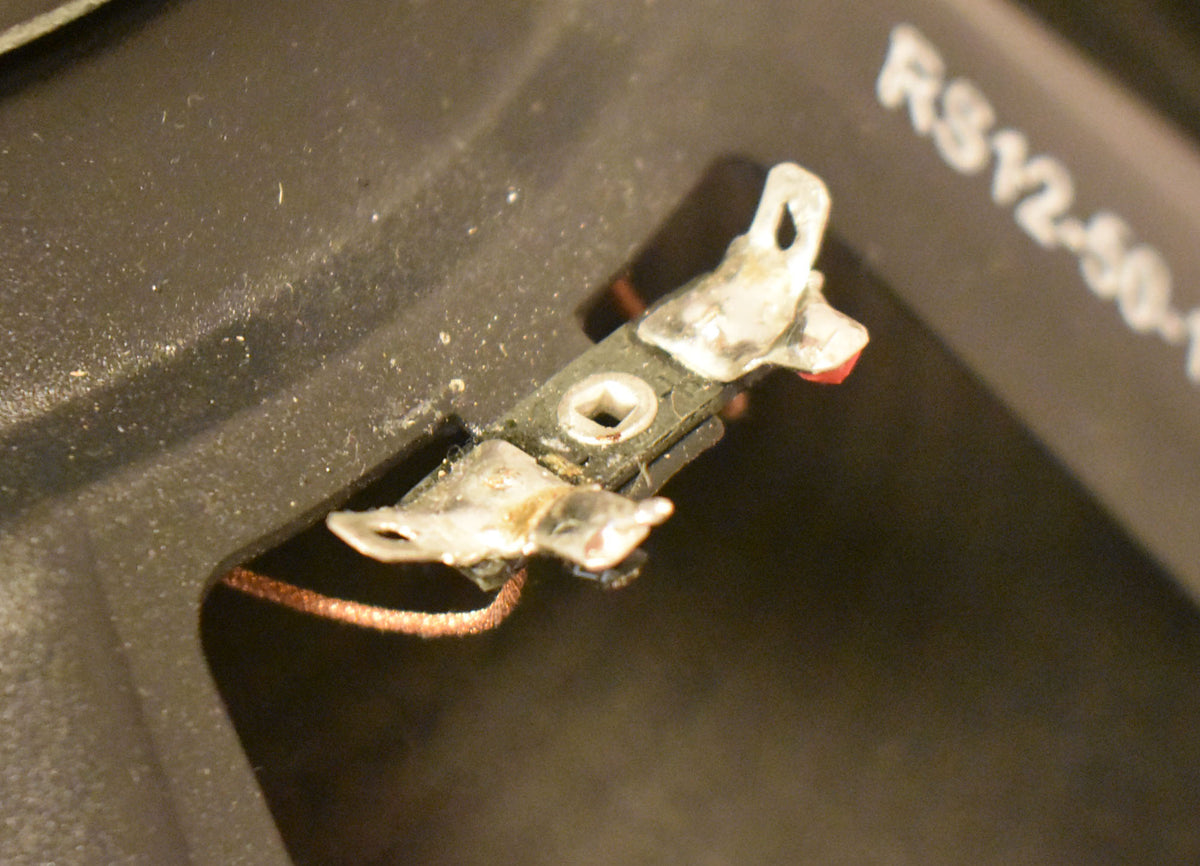 Close-up of the speaker's black frame, showing a silver-soldered terminal with a red wire and a copper wire leading into the cone.