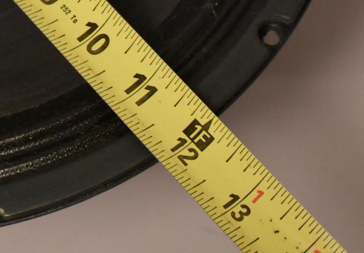 A yellow measuring tape diagonally crosses the dark gray speaker, showing its 12-inch diameter.