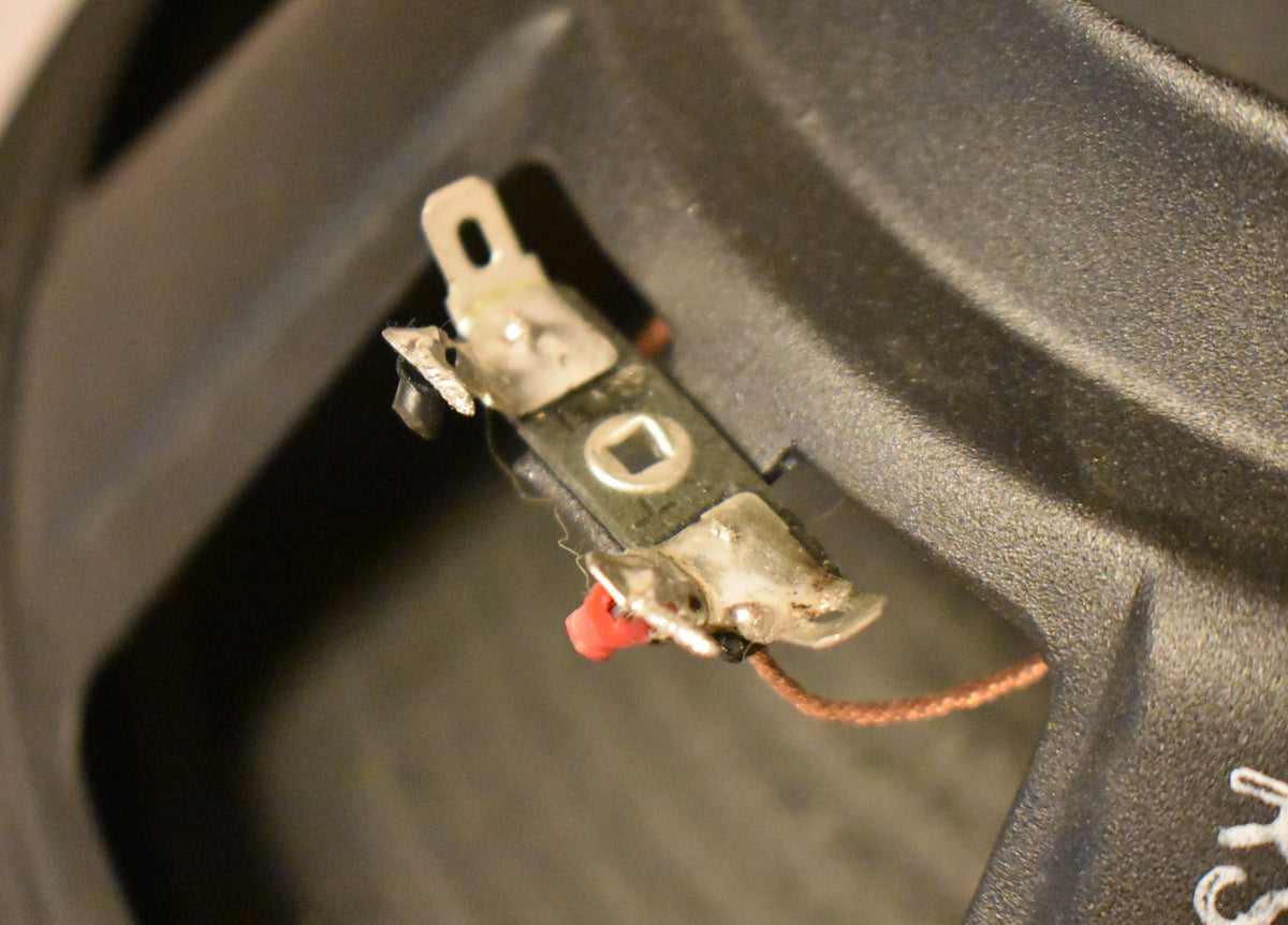 Close-up of the speaker's black textured frame, showing a silver terminal strip with a red wire connected.