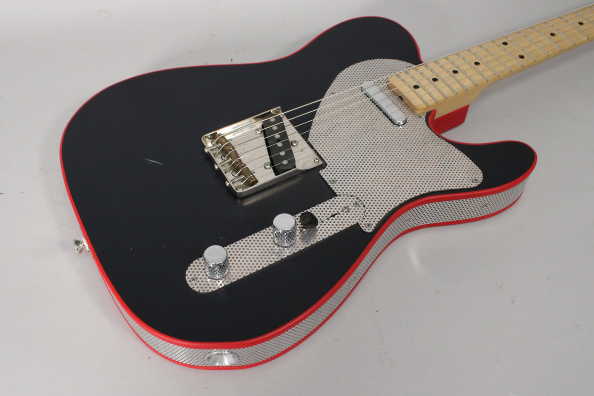 Matte black guitar body with red binding and perforated metal pickguard and side wrap, angled from the lower bout showing the bridge and controls.