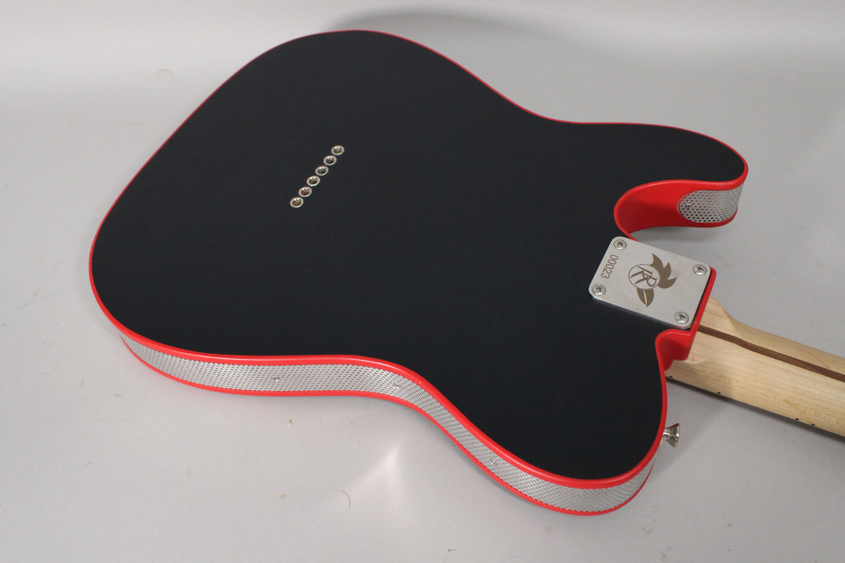 The guitar's matte black body, with red trim and silver mesh sides, is seen from the back, angled to show the neck plate and string ferrules.
