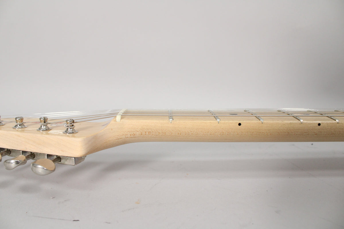 The guitar's light wood neck and headstock are viewed from the side, showing six chrome tuners and dark fret markers.