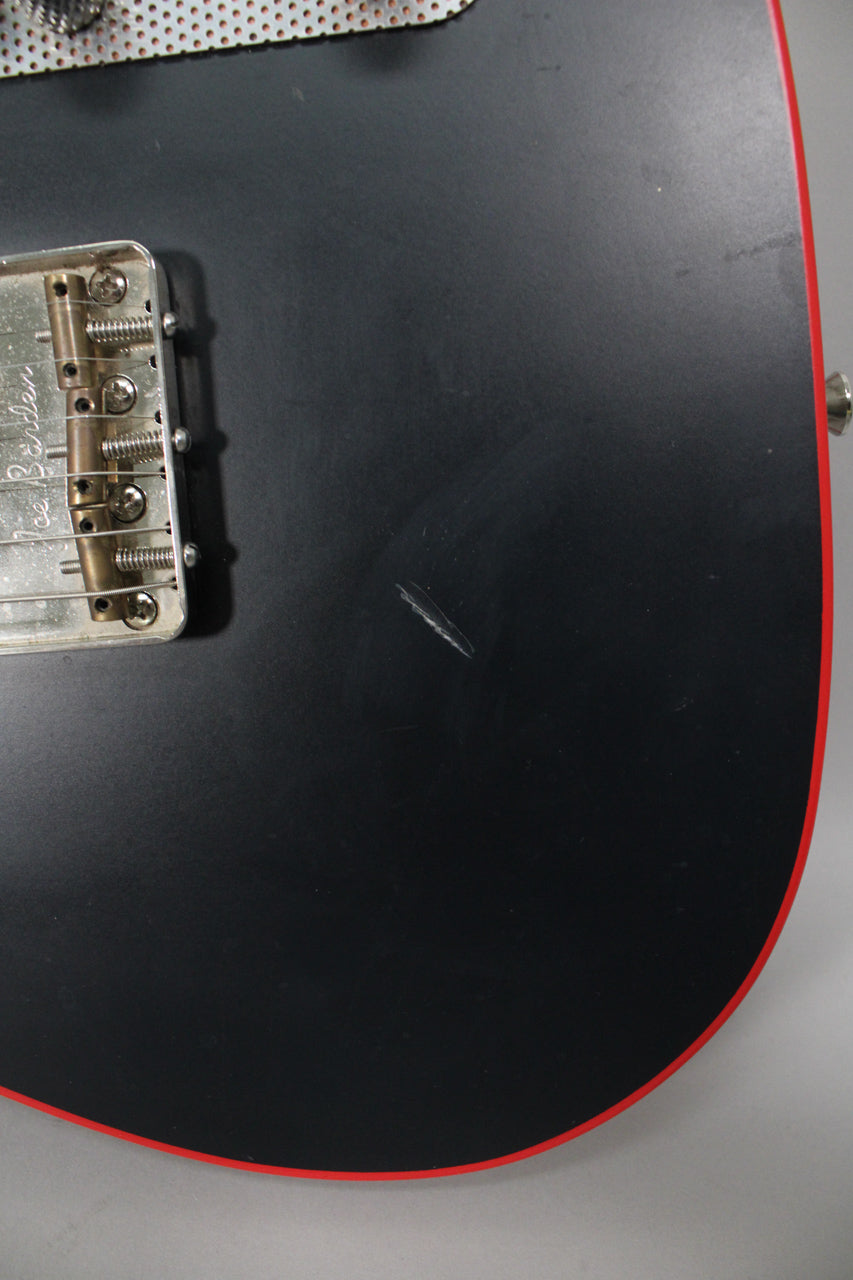 Close-up of the matte black body with red binding, showing a large scratch below the bridge and a chrome output jack.