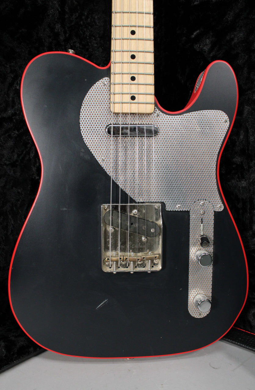 Close-up of the matte black guitar body with red binding, showing a perforated metal pickguard and control plate, and a maple fretboard.