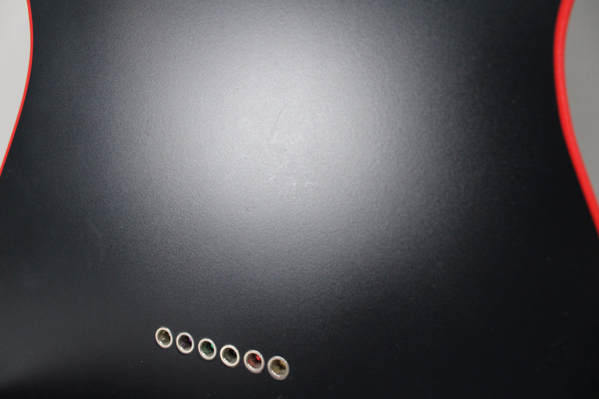 Close-up of the matte black guitar body's back, showing six chrome string ferrules and light scuffing on the finish.