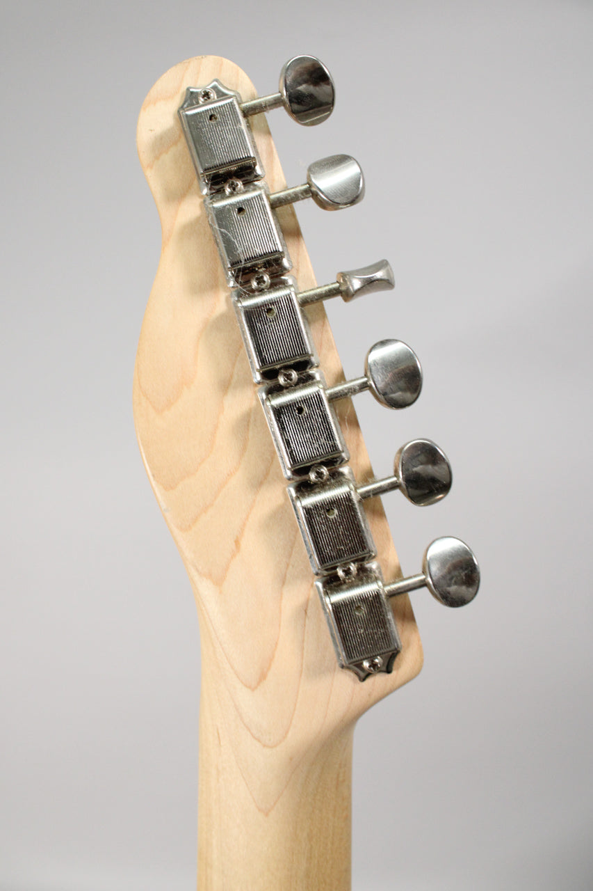 The guitar's light wood headstock and neck are visible from the back, with six chrome tuners showing some wear.