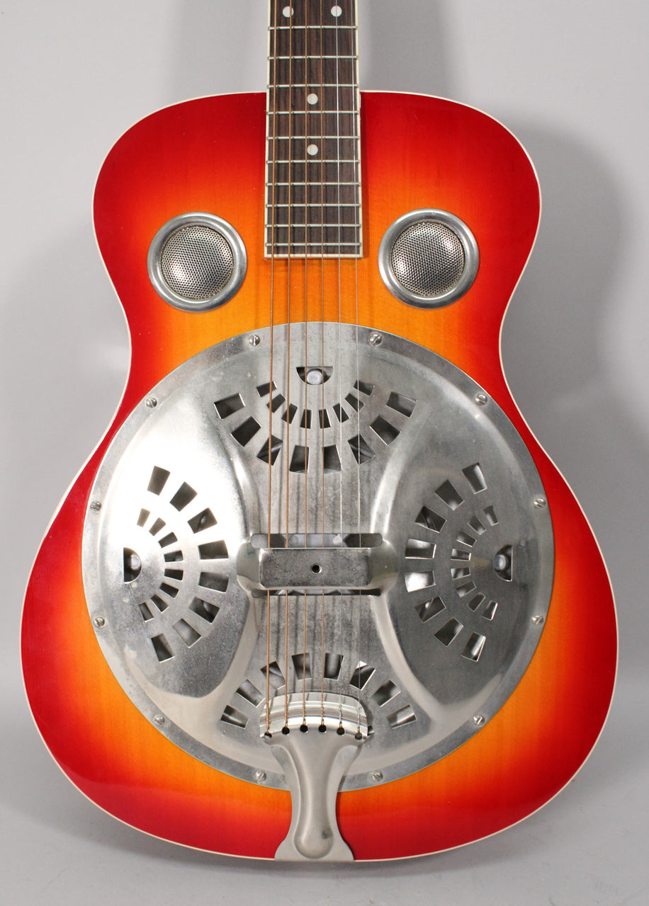Full front view of the resonator guitar, showing its cherry sunburst finish, two round soundholes, and a large, ornate metal resonator cover.