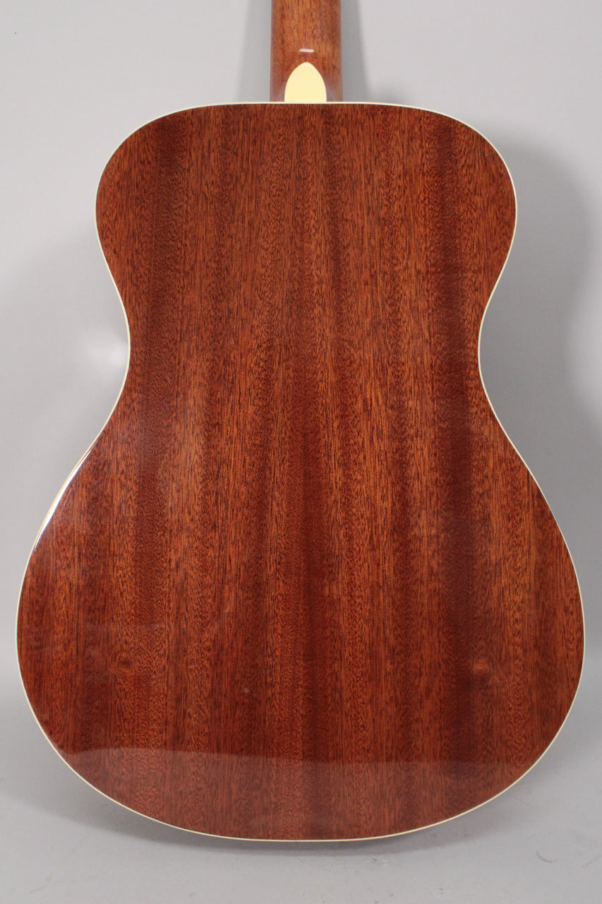 The guitar's back is shown, revealing a rich, reddish-brown wood grain with a glossy finish and cream binding.