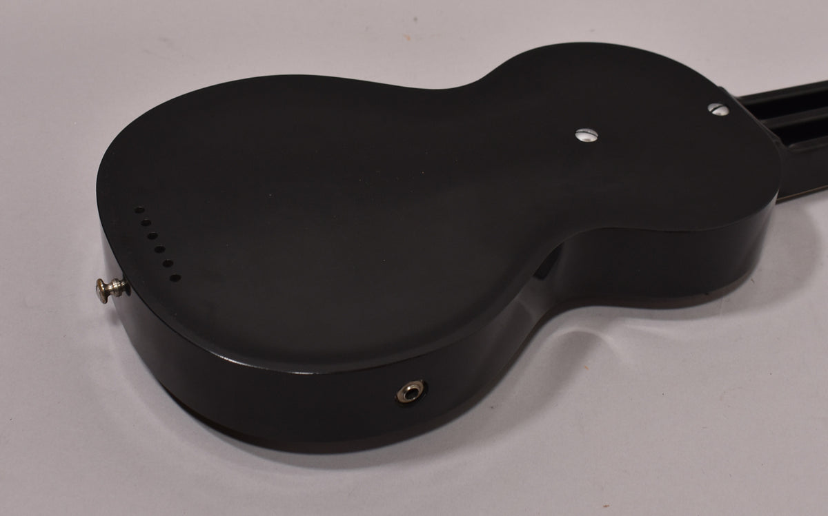 The dark, matte black lap steel's back is angled, showing a chrome strap button, output jack, and six small holes near the tail.