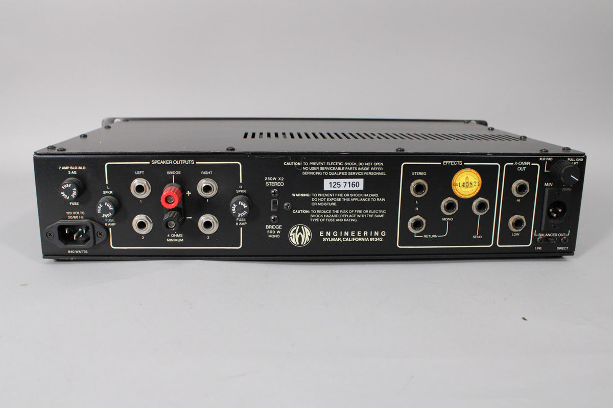The black metal amplifier's rear panel is shown, featuring numerous inputs, outputs, and controls, with a few minor scuffs.