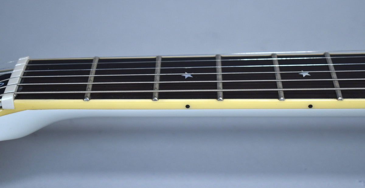 Close-up of the guitar's dark fretboard with star inlays, white binding, and side dots, showing the nut and first few frets.