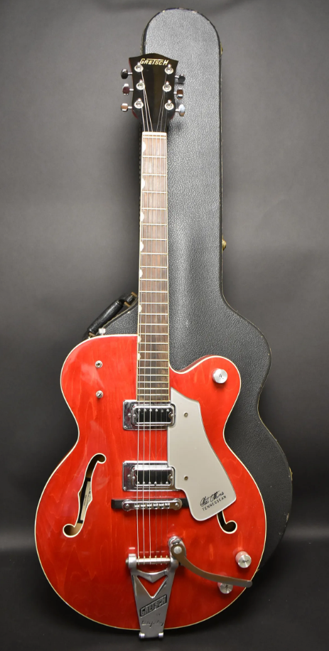 Full-length view of a cherry red hollow-body electric guitar with f-holes, a Bigsby tremolo, and a light grey pickguard.