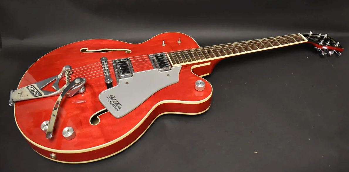 Cherry red hollow body electric guitar, angled from the lower bout, showing a Bigsby tremolo, two humbuckers, and a light gray pickguard.