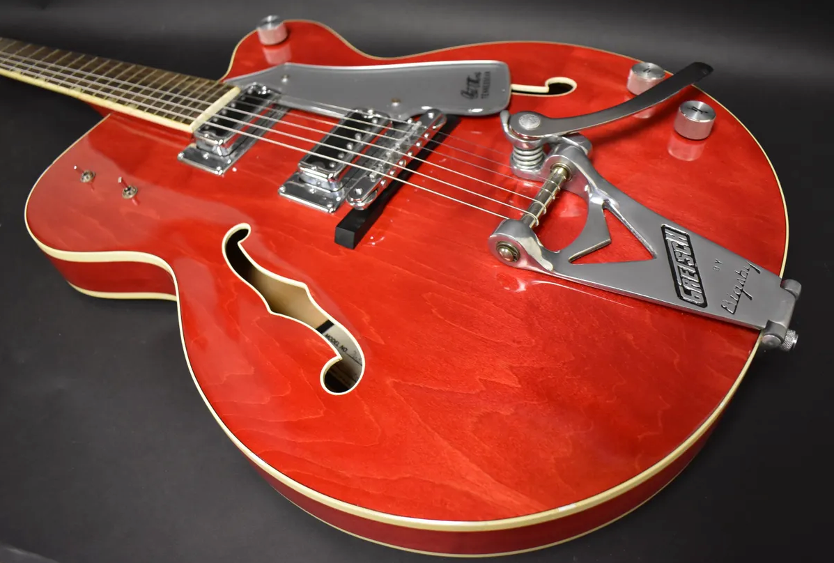 Cherry red hollow body guitar, angled from the neck, showing two chrome pickups, a Bigsby tremolo, and f-holes.