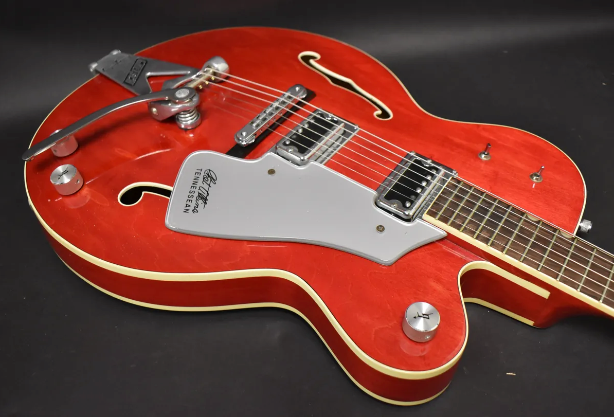Cherry red hollow-body guitar, angled from the upper bout, showing a Bigsby tremolo, two humbuckers, and a silver pickguard.