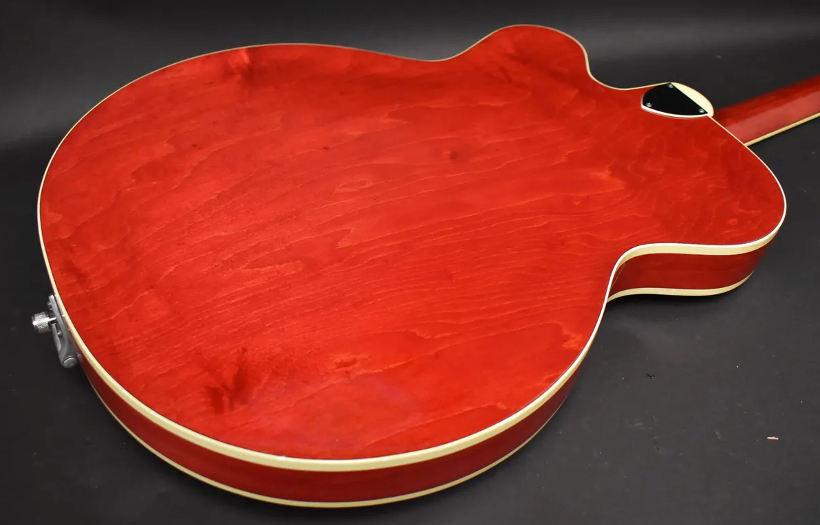 The back of a cherry red hollow-body guitar, showing wood grain, cream binding, and a strap button on the lower bout.