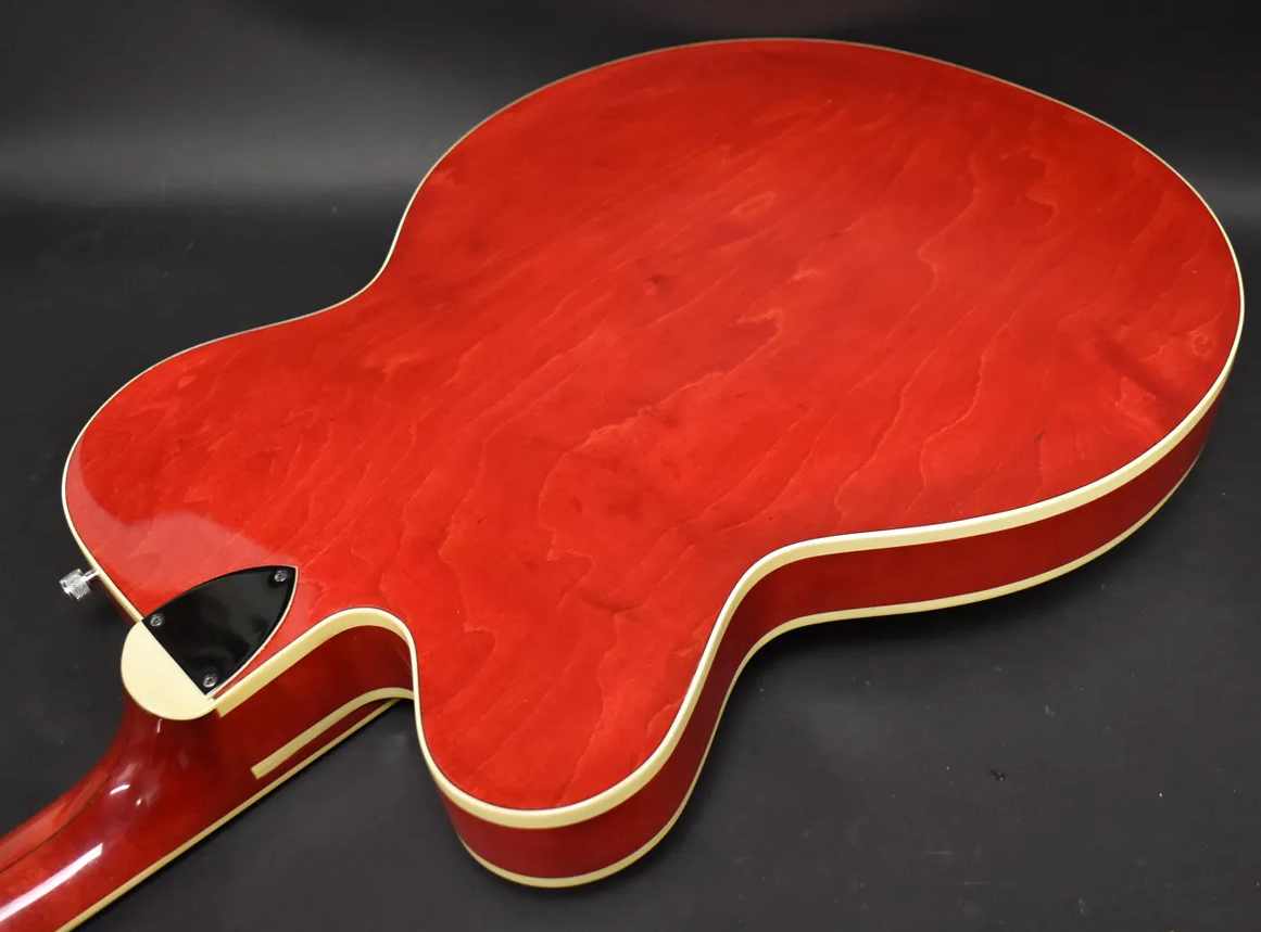 The cherry red hollow body guitar's back is angled, showing its wood grain, cream binding, and neck heel with a black cover.