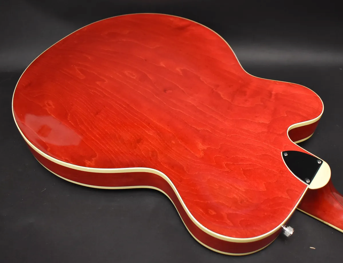 The cherry red guitar's back is angled, showing its glossy finish, wood grain, cream binding, and a black control plate near the strap button.