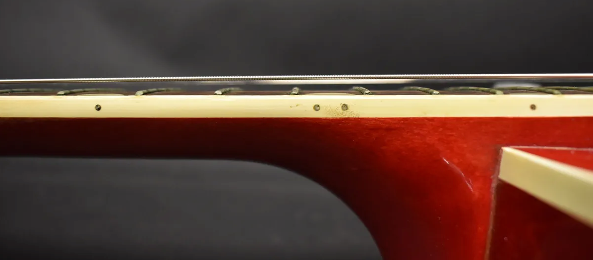 Close-up of the cherry red guitar's neck, showing cream binding with side dots and some wear near the frets.