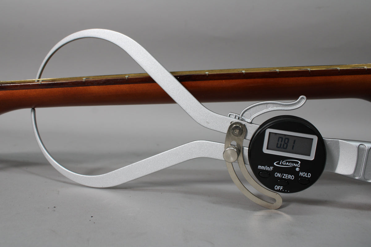 A digital caliper measures the guitar's neck thickness at 0.81 inches, showing the dark brown neck and light fretboard.