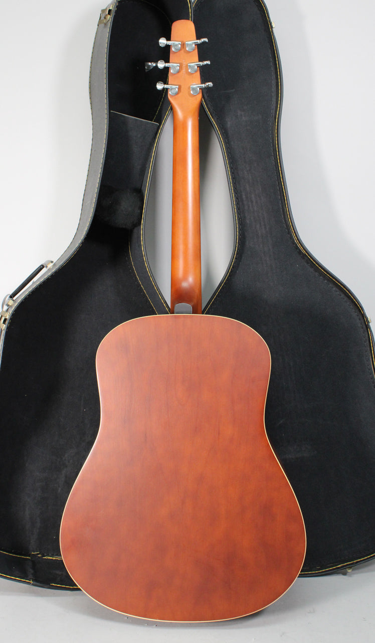 The guitar's back and neck are visible, with a matte reddish-brown finish, chrome tuners, and a black hard case behind it.