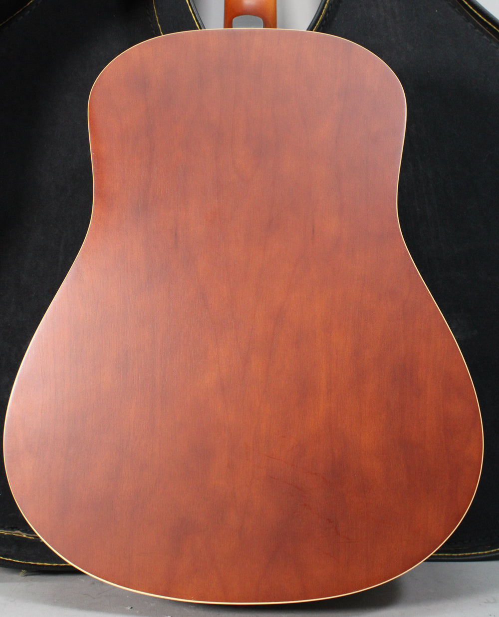 Full view of the guitar's reddish-brown back with a matte finish, showing subtle wood grain and light binding around the edges.