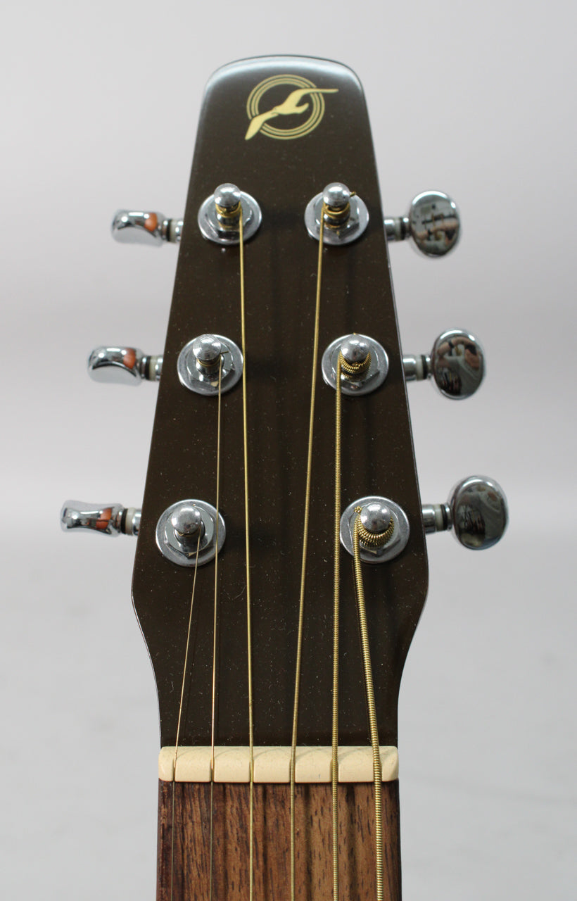 Close-up of the dark brown headstock with a gold logo, six chrome tuners, and a cream nut, showing the top of the fretboard.