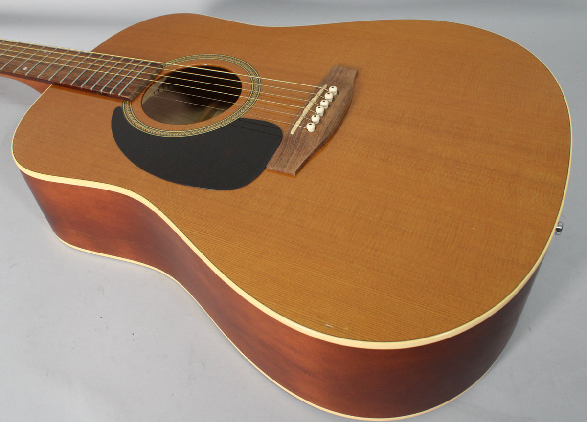 The left-handed acoustic guitar's cedar top and mahogany sides are visible from the upper bout, with a black pickguard.