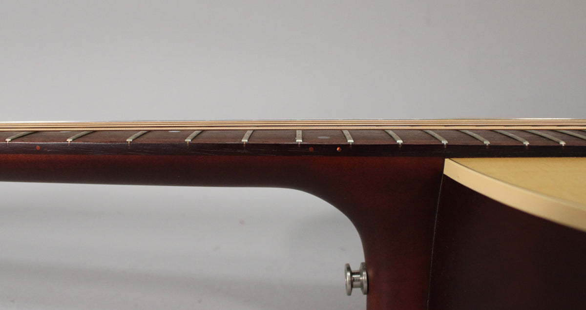 Side view of the guitar neck and upper body, showing the dark fretboard with light fret markers and a strap button.