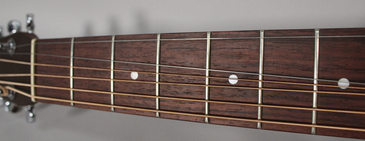 Close-up of the dark brown fretboard with white dot inlays, showing light strings and silver frets, from the nut to the 7th fret.