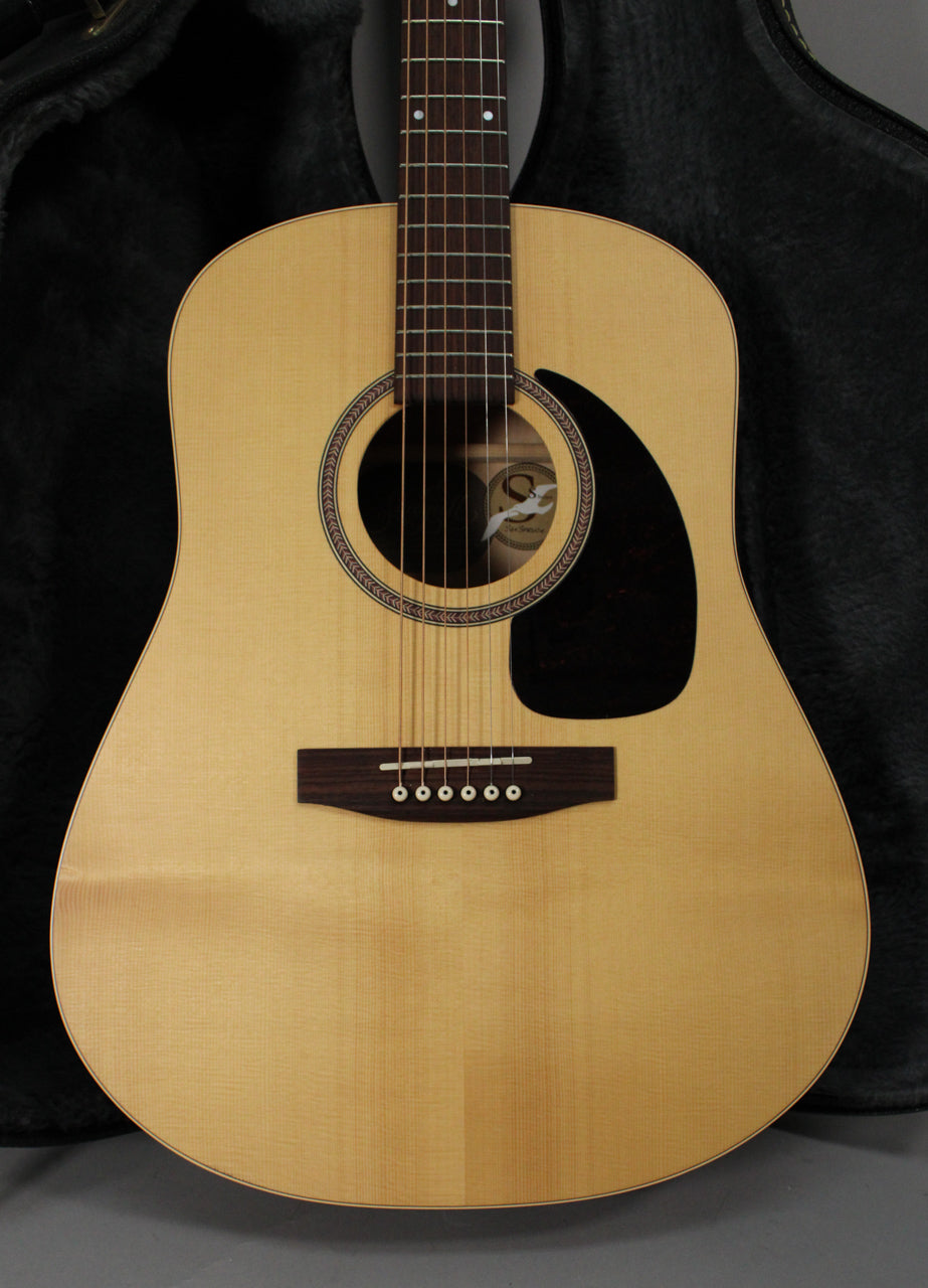 Full front view of a light blonde acoustic guitar with a dark fretboard, black pickguard, and decorative rosette.