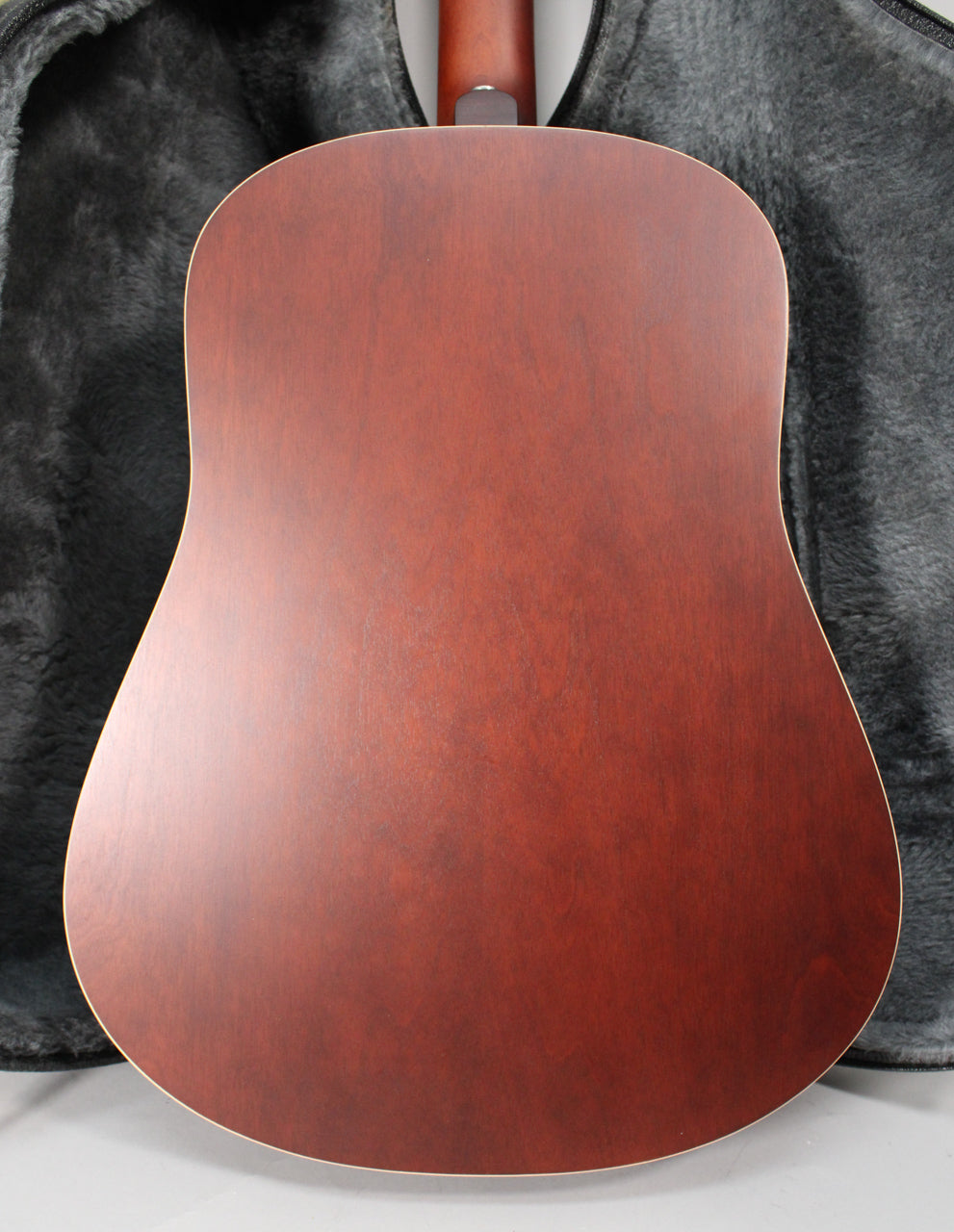 The guitar's back is a solid reddish-brown, matte finish, with a light binding visible along the edges, resting in a dark grey case.