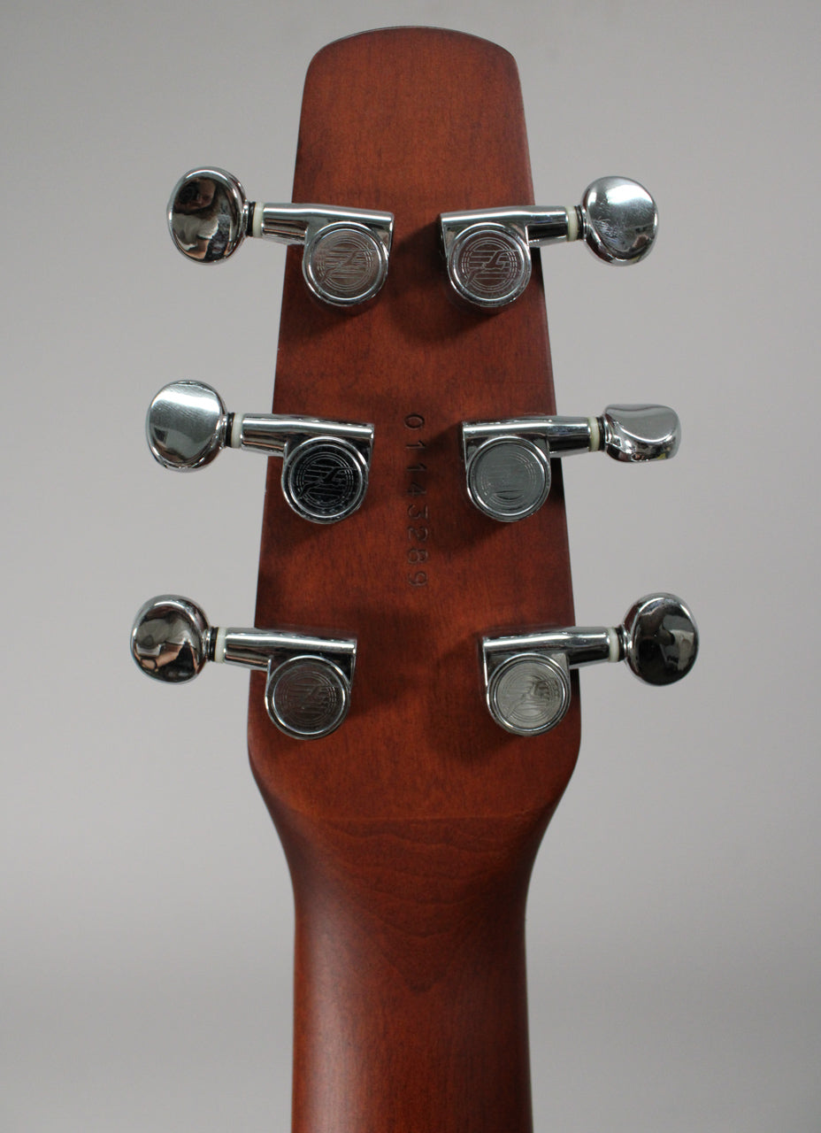 The back of a guitar headstock and top of the neck, showing six chrome tuners with oval buttons and a faint serial number.