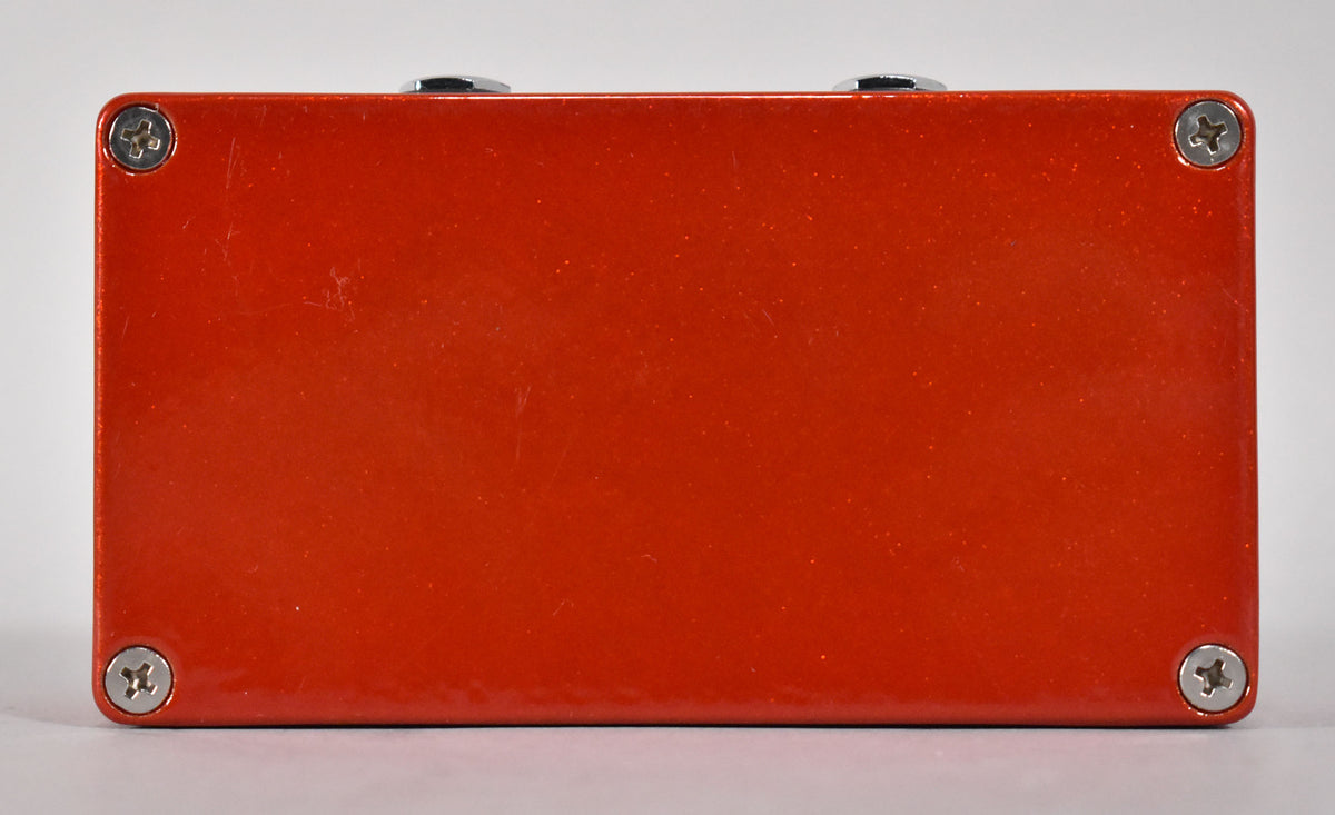 The top of a metallic orange pedal with visible surface scratches, showing two chrome knobs and four silver screws.