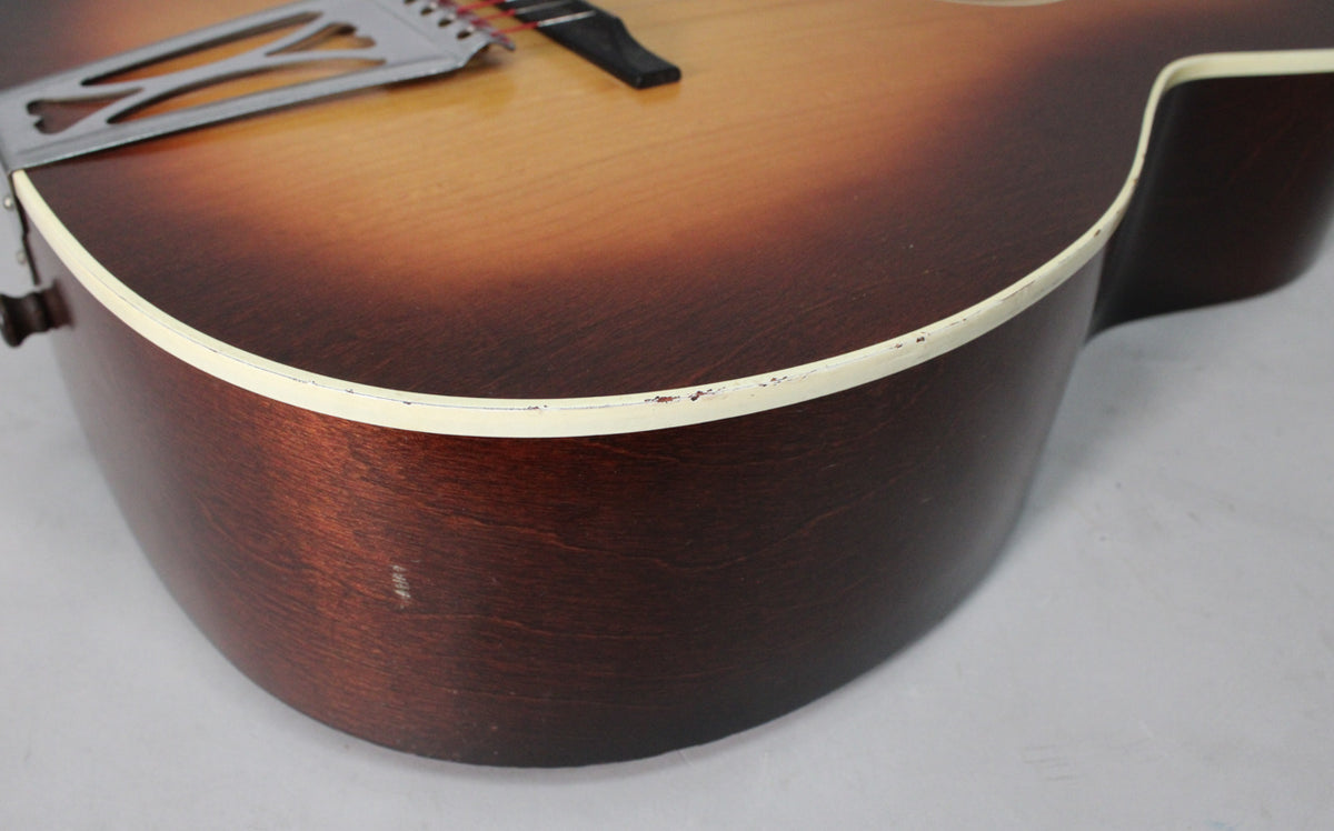 Close-up of the sunburst acoustic guitar's lower bout, showing wear and chips along the cream binding and a scratch on the dark brown side.