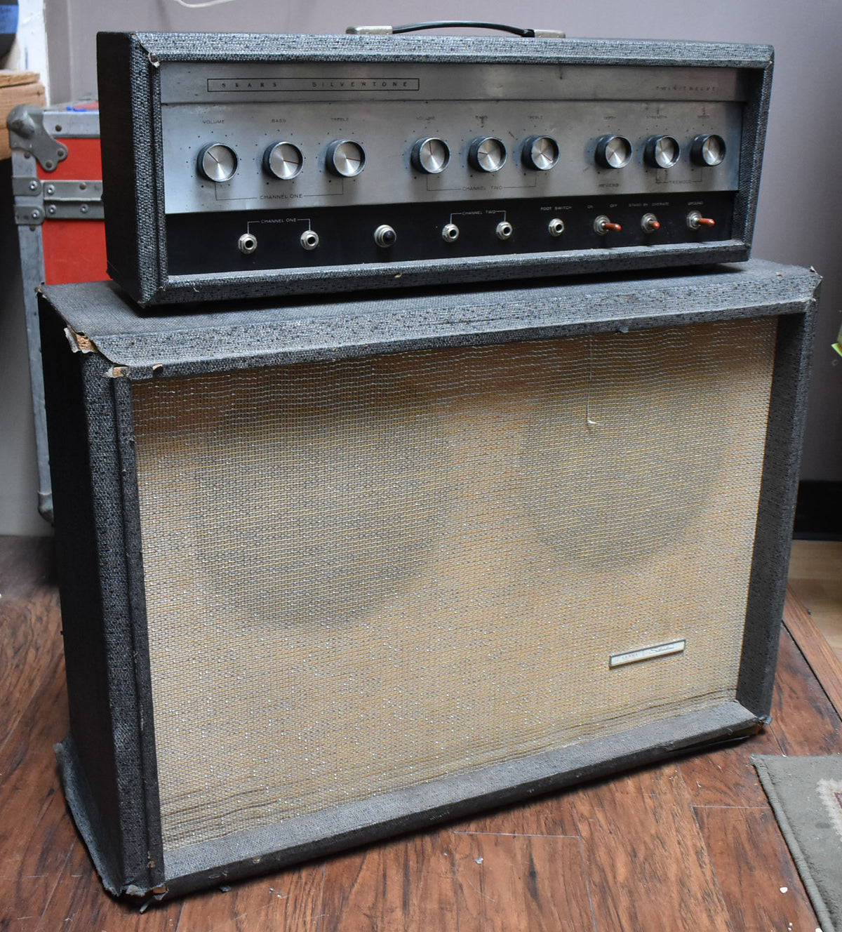 Full view of the gray textured amp head with 8 silver knobs and 4 red toggle switches, sitting atop the matching speaker cabinet with a tan grille cloth.