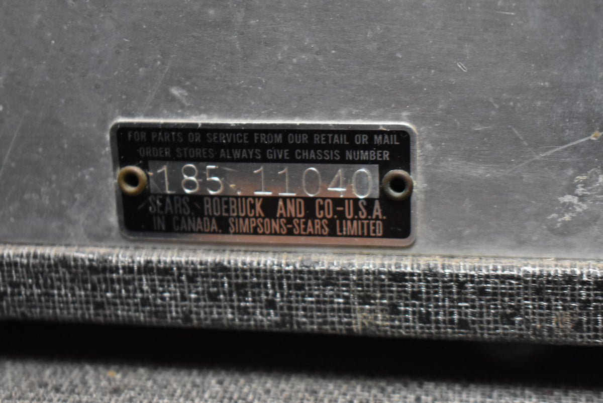 Close-up of the amp's metal chassis with a black serial number plate, showing wear and scuffs on the silver finish and black tolex.