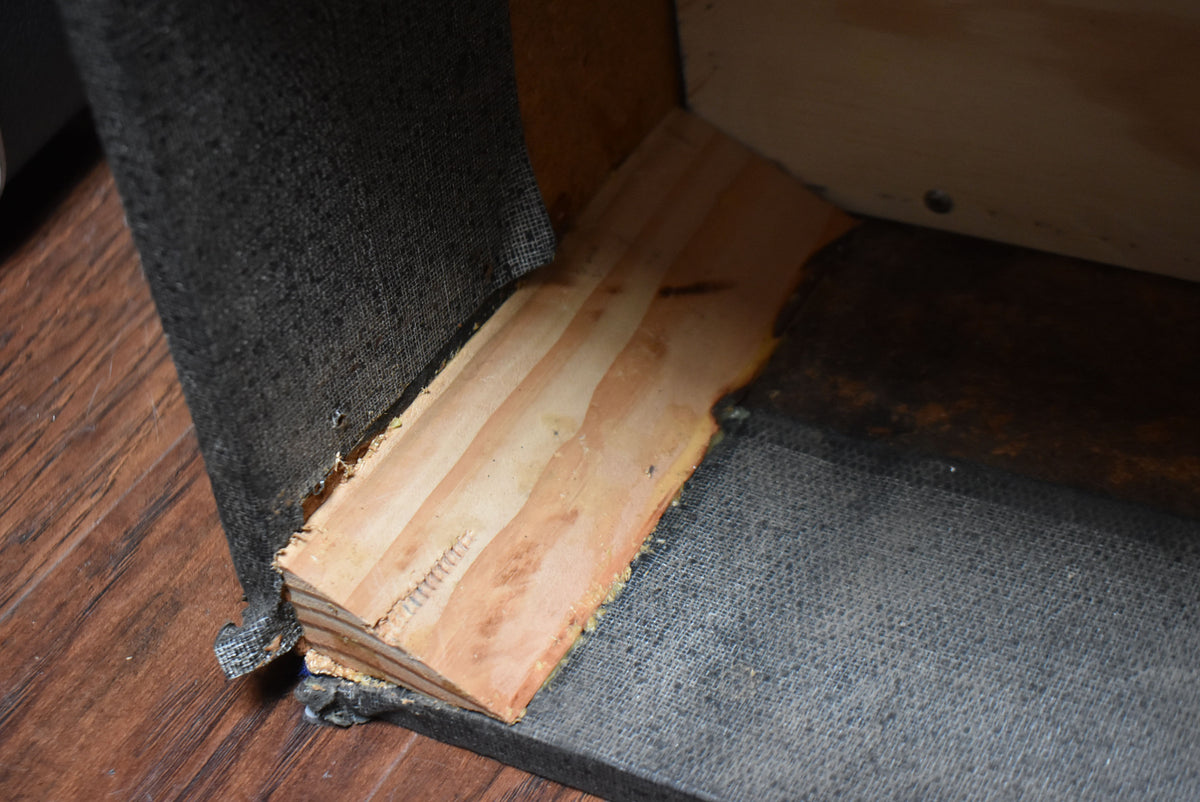 Close-up of the amp's bottom corner, showing worn black tolex, exposed light wood, and a dark, textured interior.