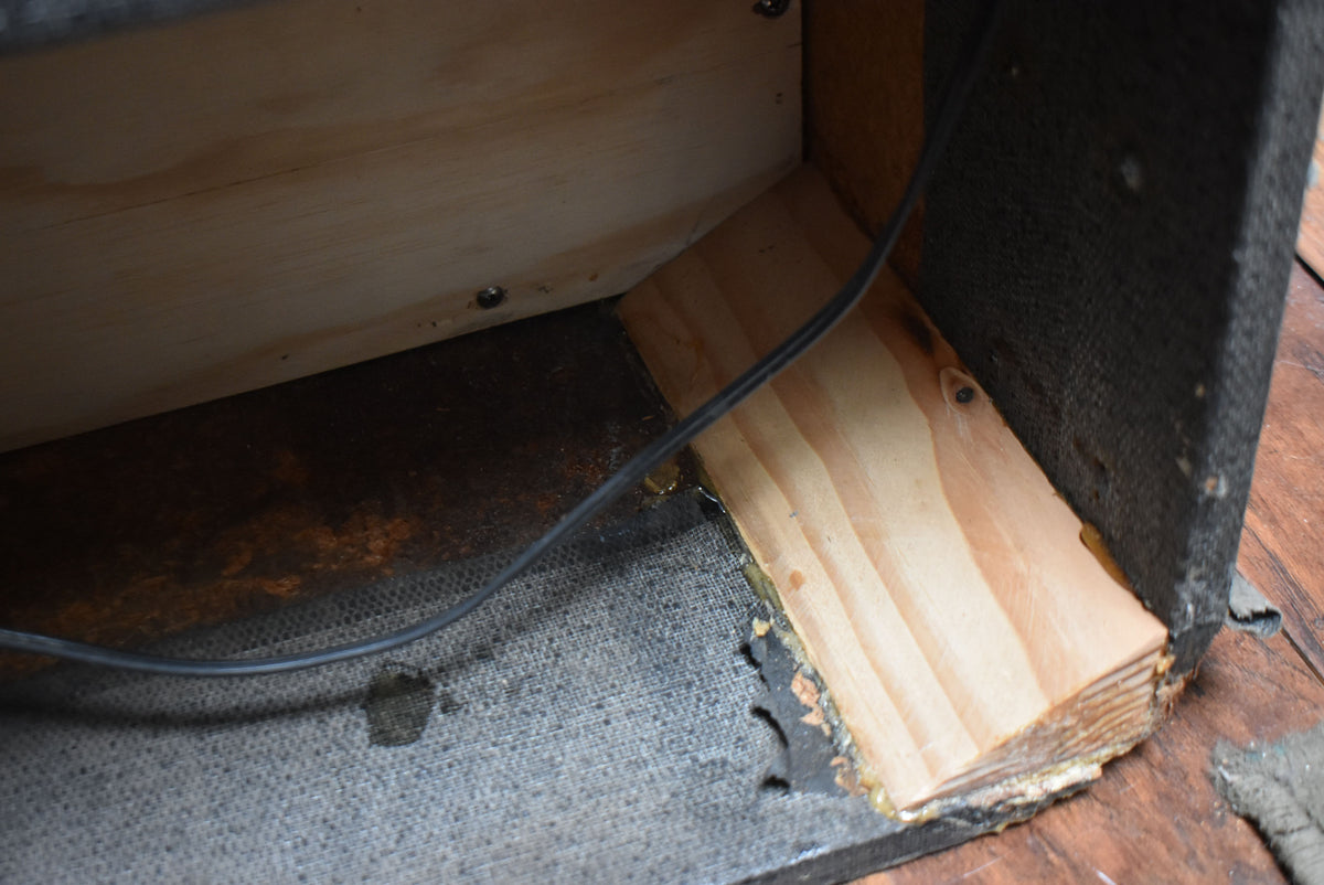 Close-up of the cabinet's interior, showing exposed light wood, a black cable, and worn dark gray tolex with tears and rust.