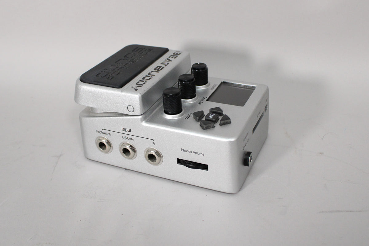 A silver drum machine pedal, angled to show the input jacks, three black control knobs, a small screen, and four triangular buttons.