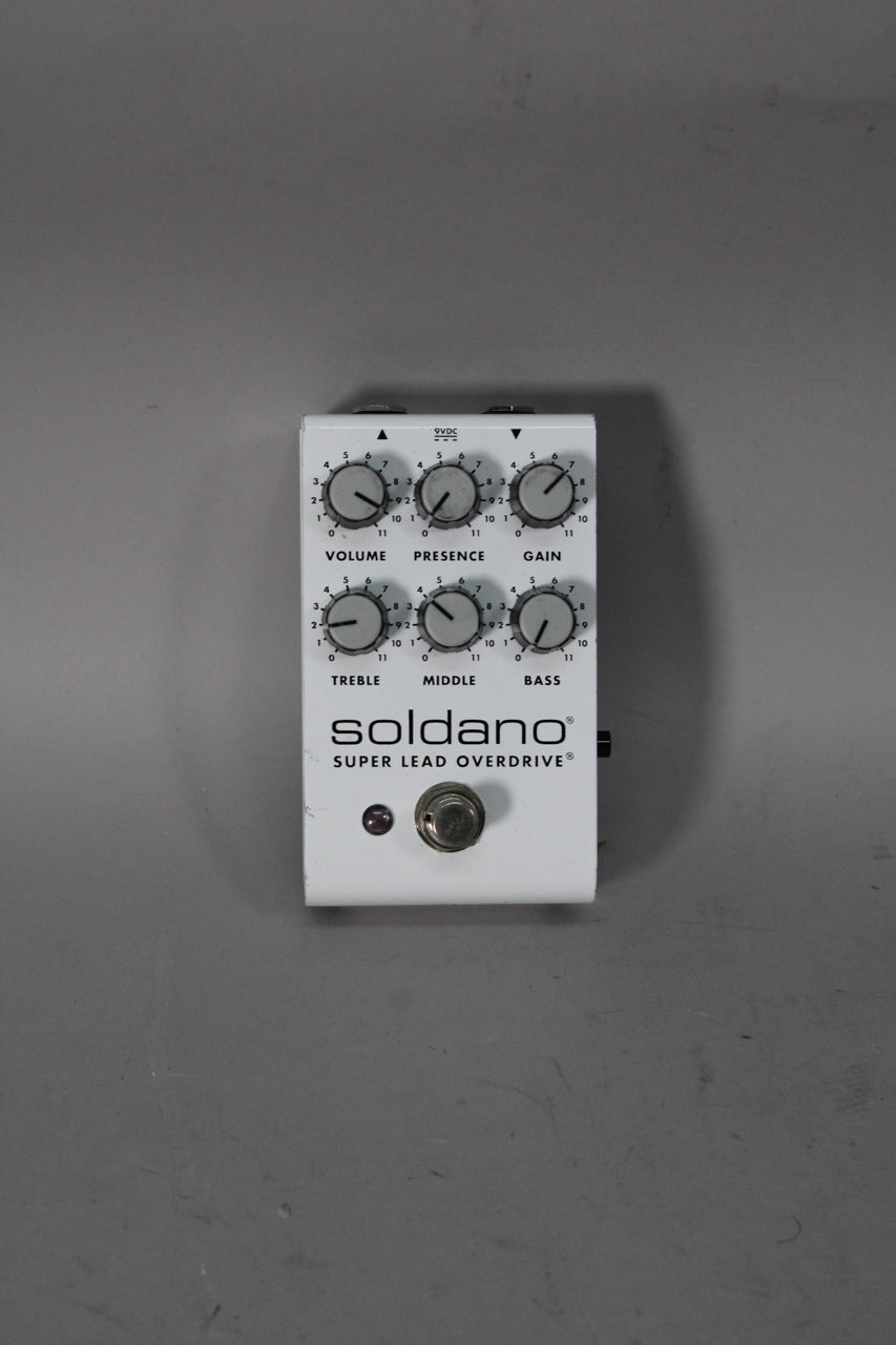 White rectangular pedal with six black-numbered grey knobs, a red LED, and a silver footswitch, viewed from above.