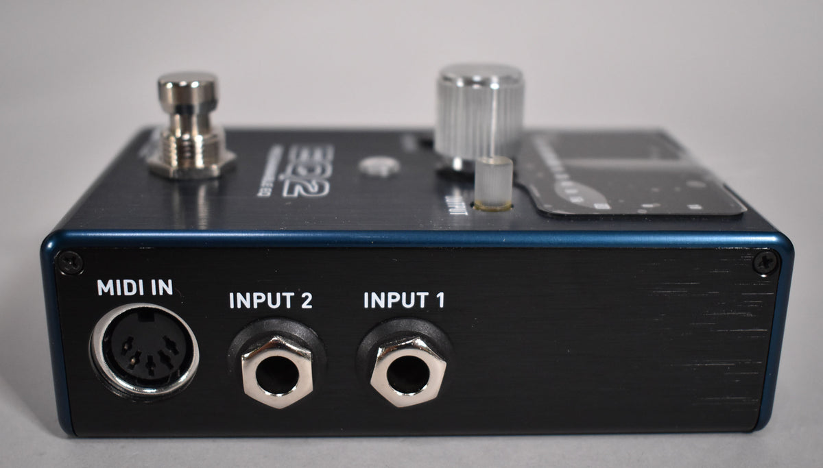 The pedal's rear panel, with a MIDI IN port and two 1/4-inch input jacks, is visible below a dark blue top with silver controls.