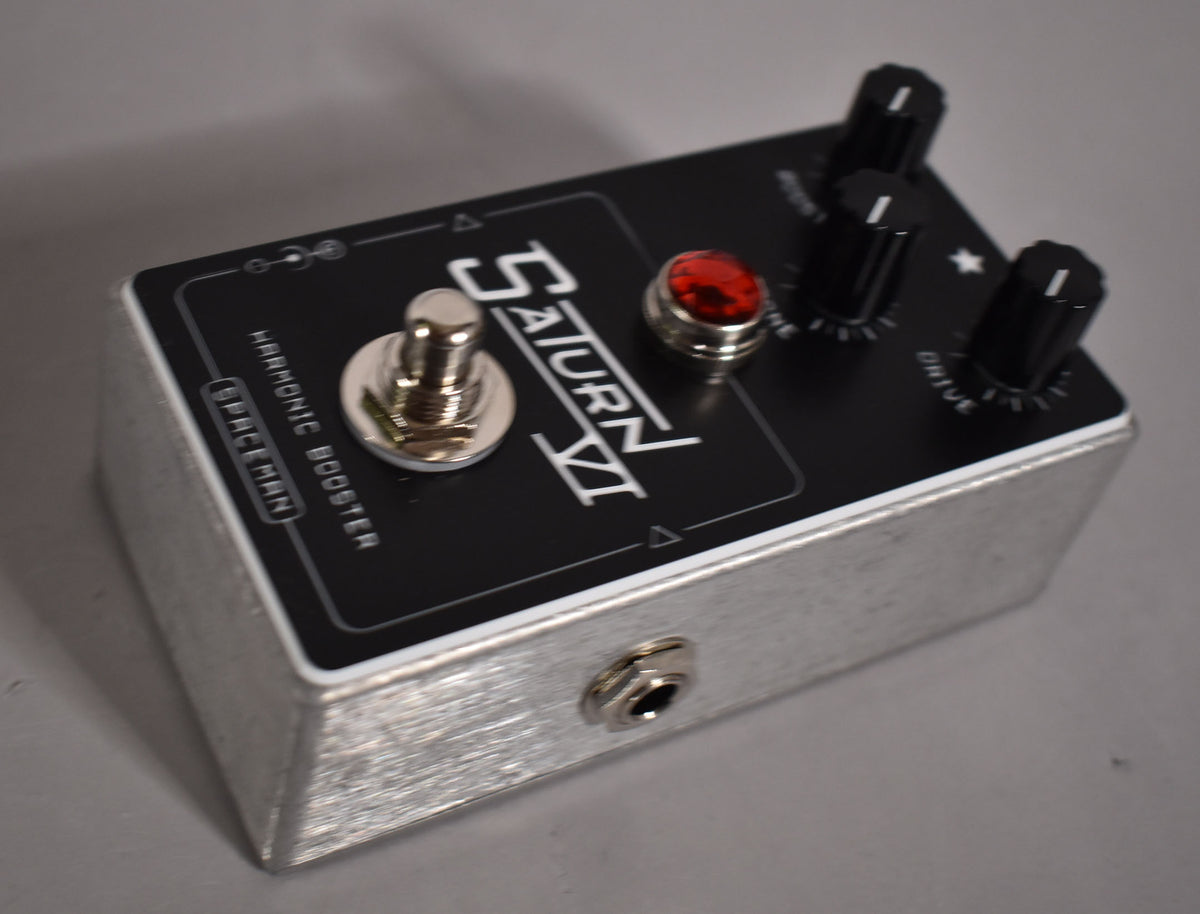 A silver guitar pedal with a black top panel, a chrome toggle switch, a red jewel light, and three black control knobs.