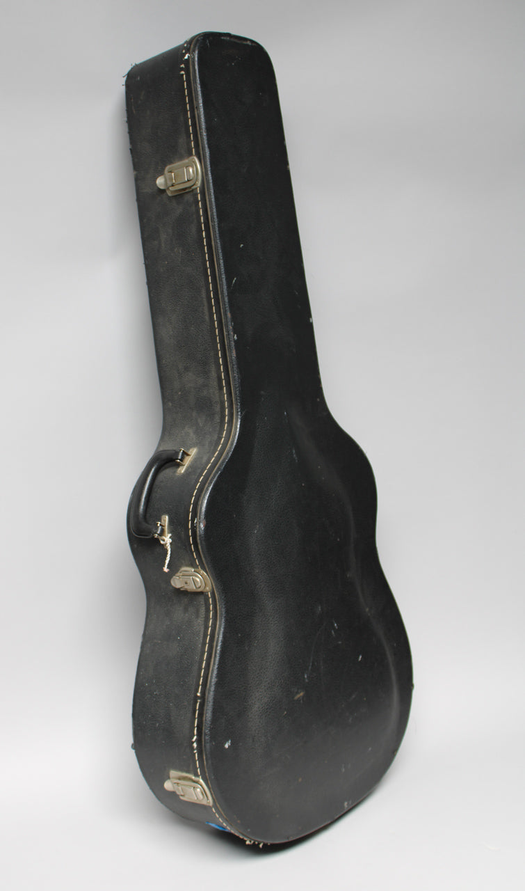 A black archtop guitar case with white stitching, brass-colored latches, and a black handle, viewed from the front at an angle.