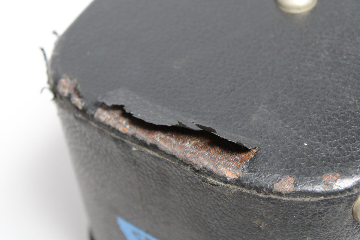 Close-up of the black case's corner, showing significant tears in the covering exposing the reddish-brown material underneath.