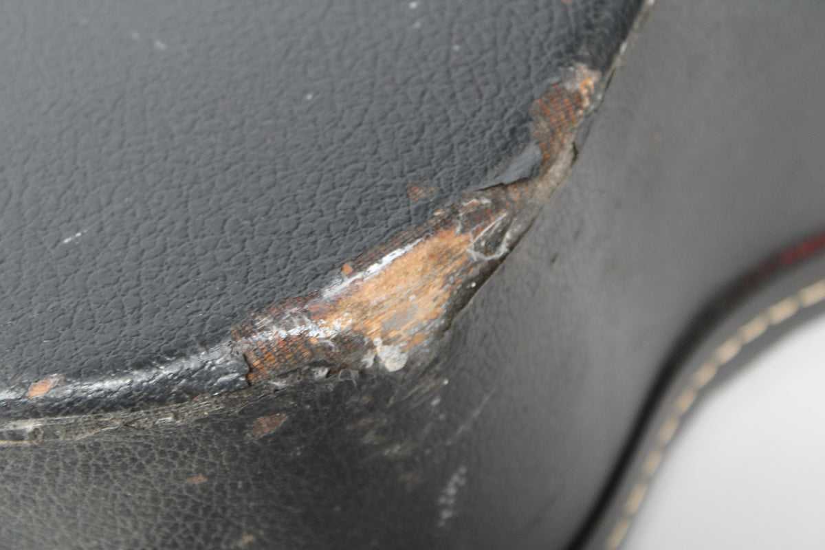Close-up of the black archtop case's corner, showing significant wear with exposed wood and peeling Tolex.