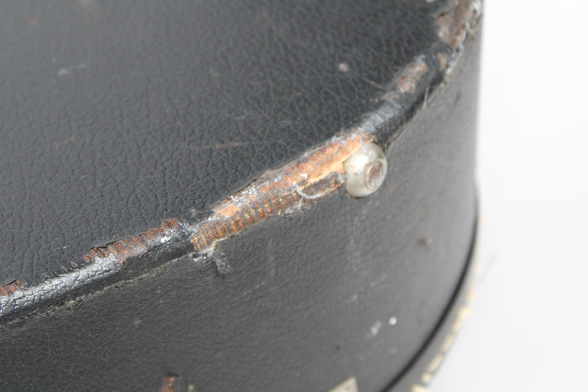 Close-up of the black archtop case's worn binding, revealing the brown wood underneath, with a silver rivet visible.