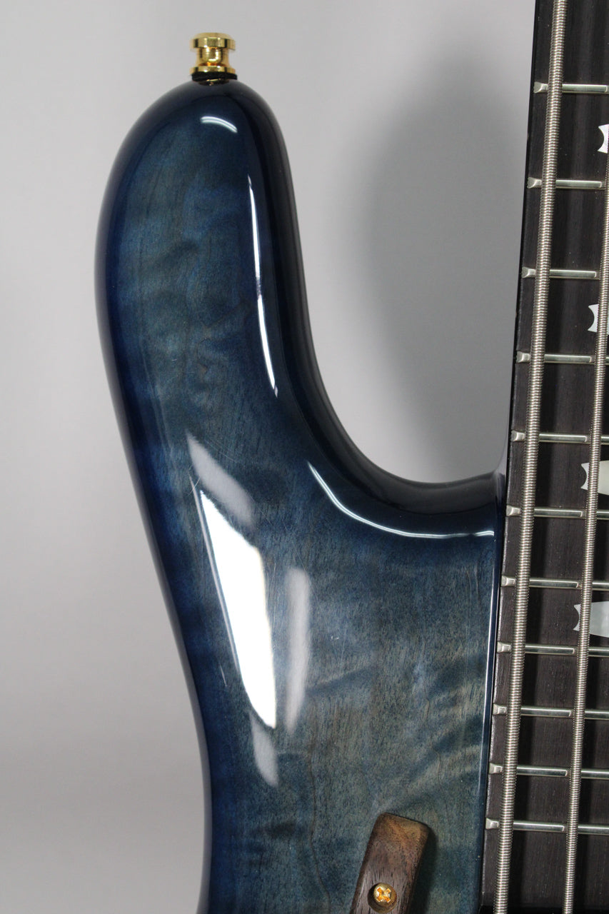 Close-up of the bass's upper horn in blue fade gloss, showing wood grain, a gold strap button, and part of the fretboard.