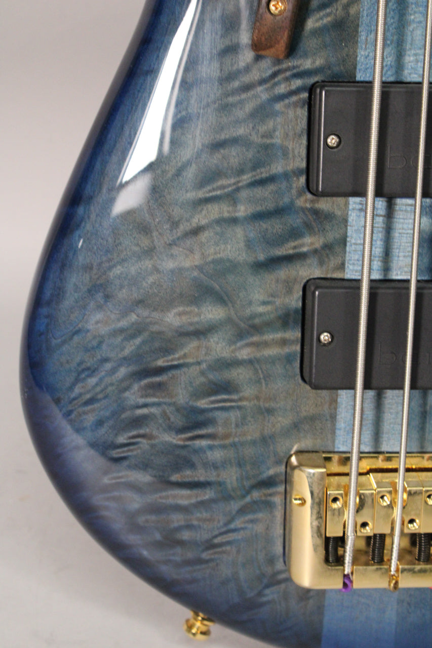 Close-up of the bass body's lower bout, showing the blue fade gloss finish with wood grain, two black pickups, and a gold bridge.