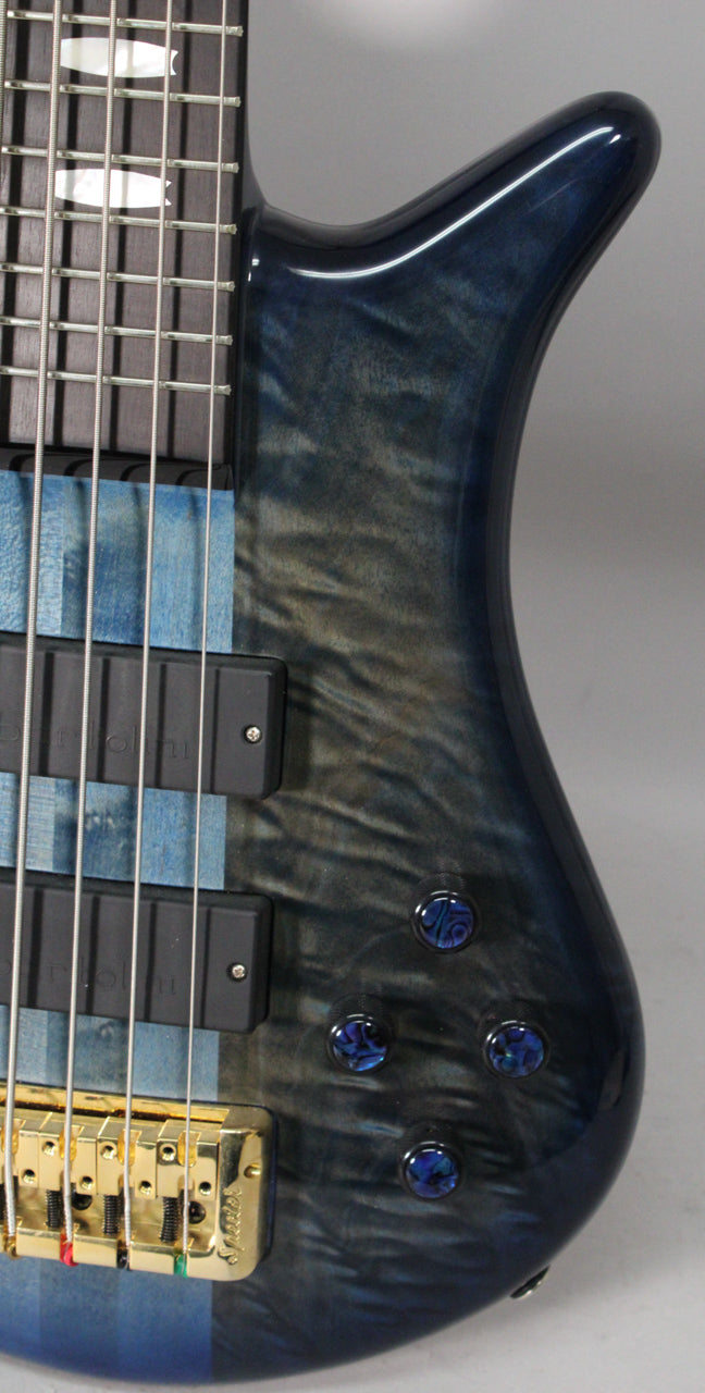 Close-up of the bass body's upper bout, showing the blue fade gloss finish, two black pickups, four blue abalone control knobs, and a gold bridge.